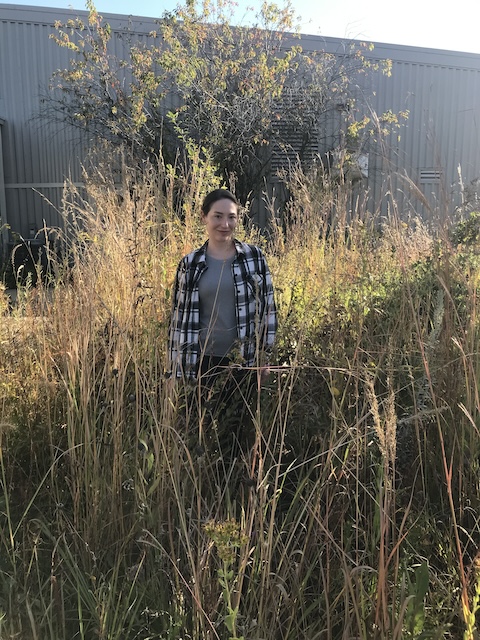 Photo of Jennifer Young in tall prairie grass in front of part of the Tallgrass Prairie Center building