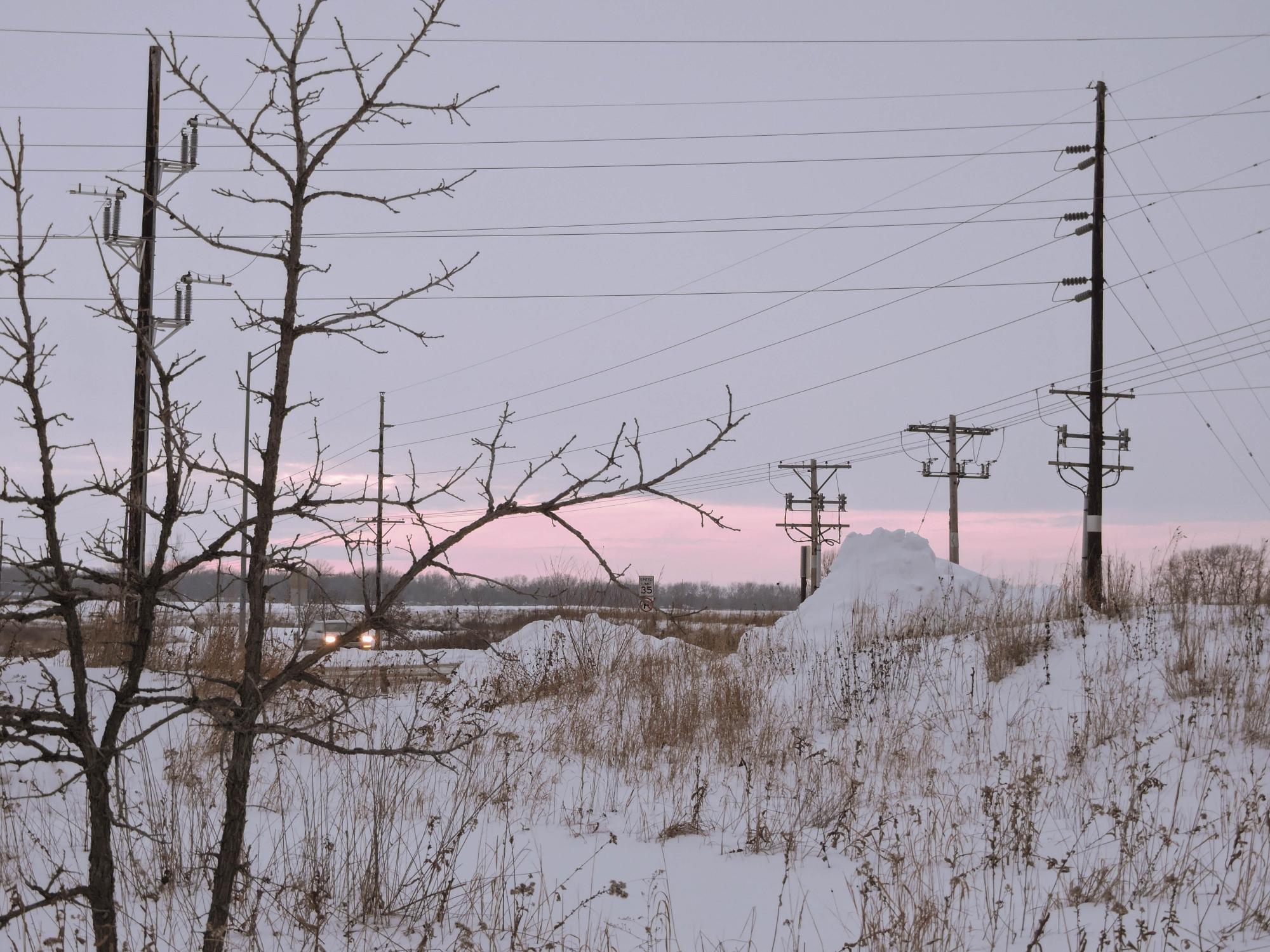 Heavy snow accumulation covers native prairie vegetation in a roadside at sunrise.
