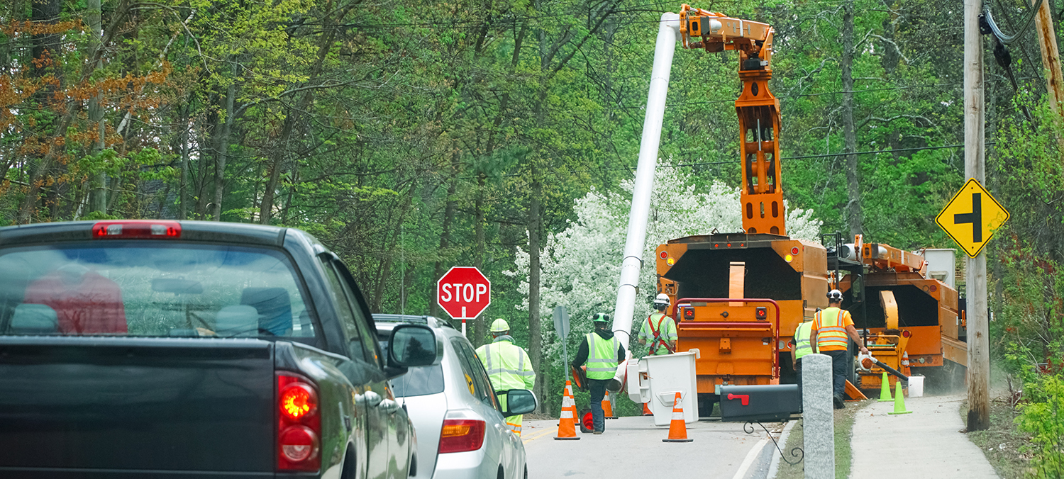Orange bucket truck and wood chipping equipment while staff work to control traffic stopped behind the equipment.