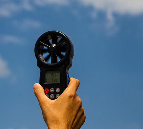 A hand holds a handheld anemometer in the air to measure weather conditions before a controlled burn.