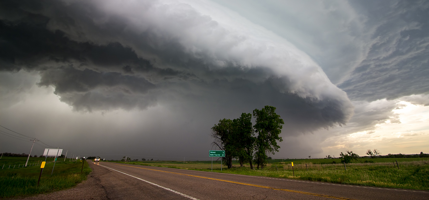 Massive storm clouds and a dark sky over a rural paved road.