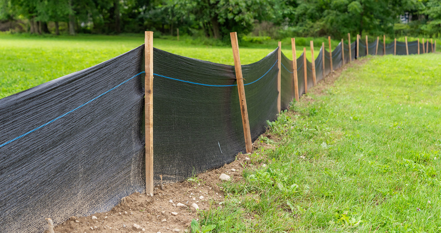 A long, black silt fence in place between areas of green grass.