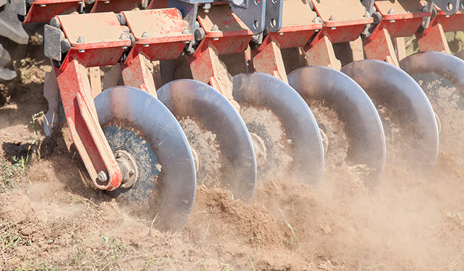 A closeup of discs ripping into dirt to create grooves.