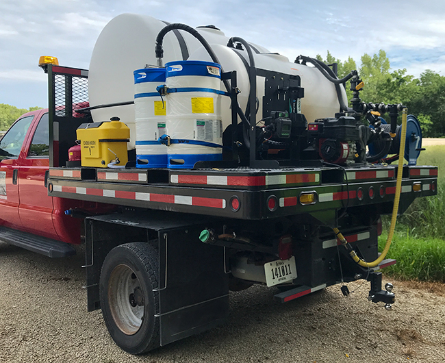 A spray system with a large tank, two smaller tanks and other equipment mounted to the flatbed of a red pickup truck.