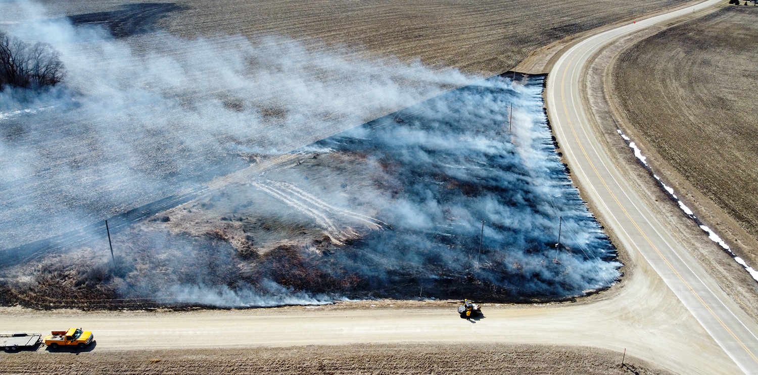 An arial photo of a roadside near an intersection that is smoldering after a controlled burn.