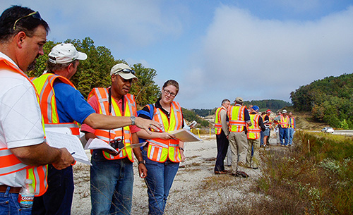 Dozens of roadside managers wearing safety vests out in a roadside learning about roadside vegetation management.