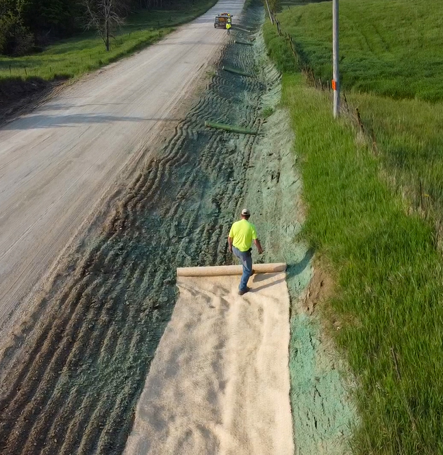 A person walks on top of an erosion control blanket that is being applied in the roadside.