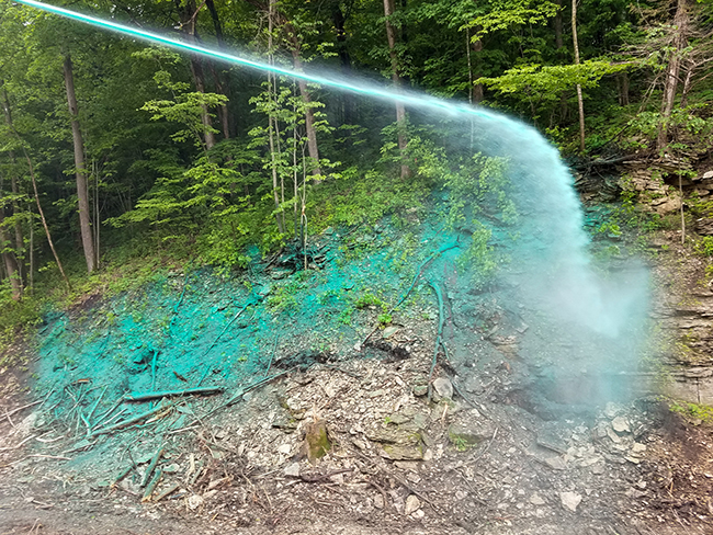 Green hydroseeding is sprayed on to a rocky sloping roadside.