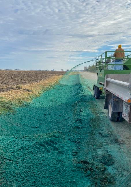 A person on a truck sprays hydroseed into the roadside.