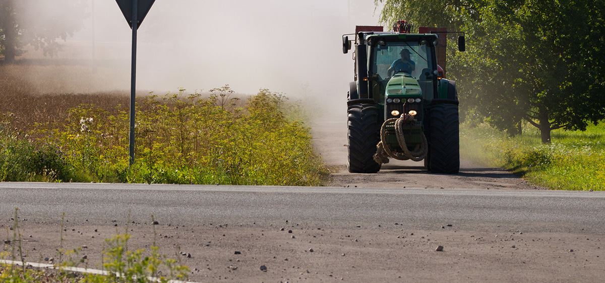 A tractor approaches the road, which has native vegetation in the roadside.