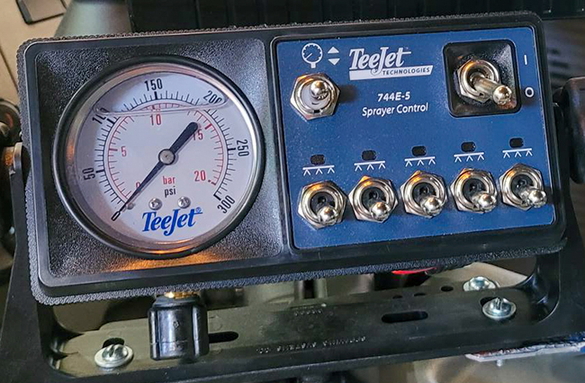 A cab-mounted console for controlling a spray system featuring various switches and a pressure gauge.