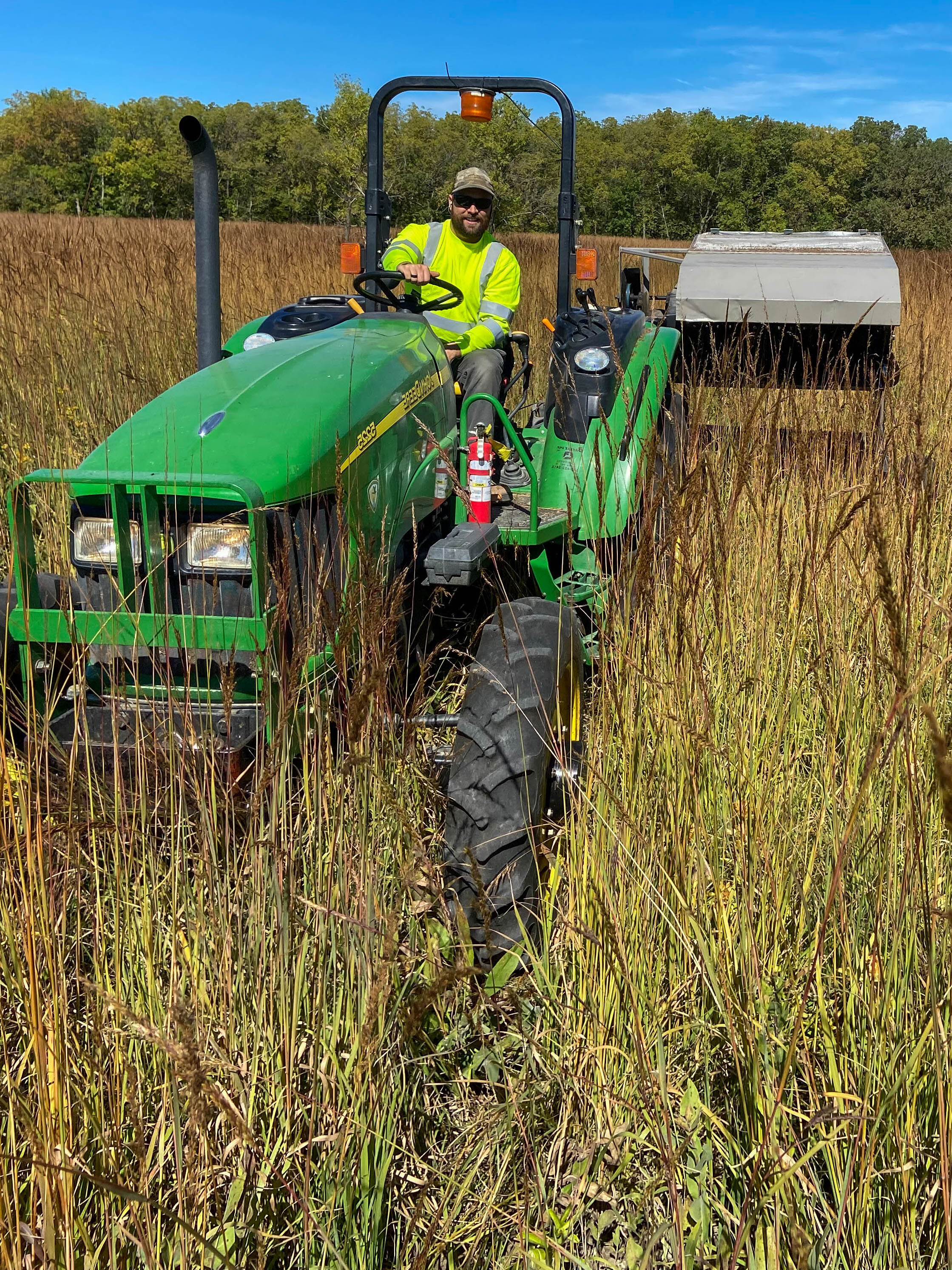 A roadside manager riding a tractor while working in prairie vegetation.
