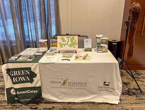 A table with brochures on top. Next to the table is a display of a long stem system from native prairie vegetation.